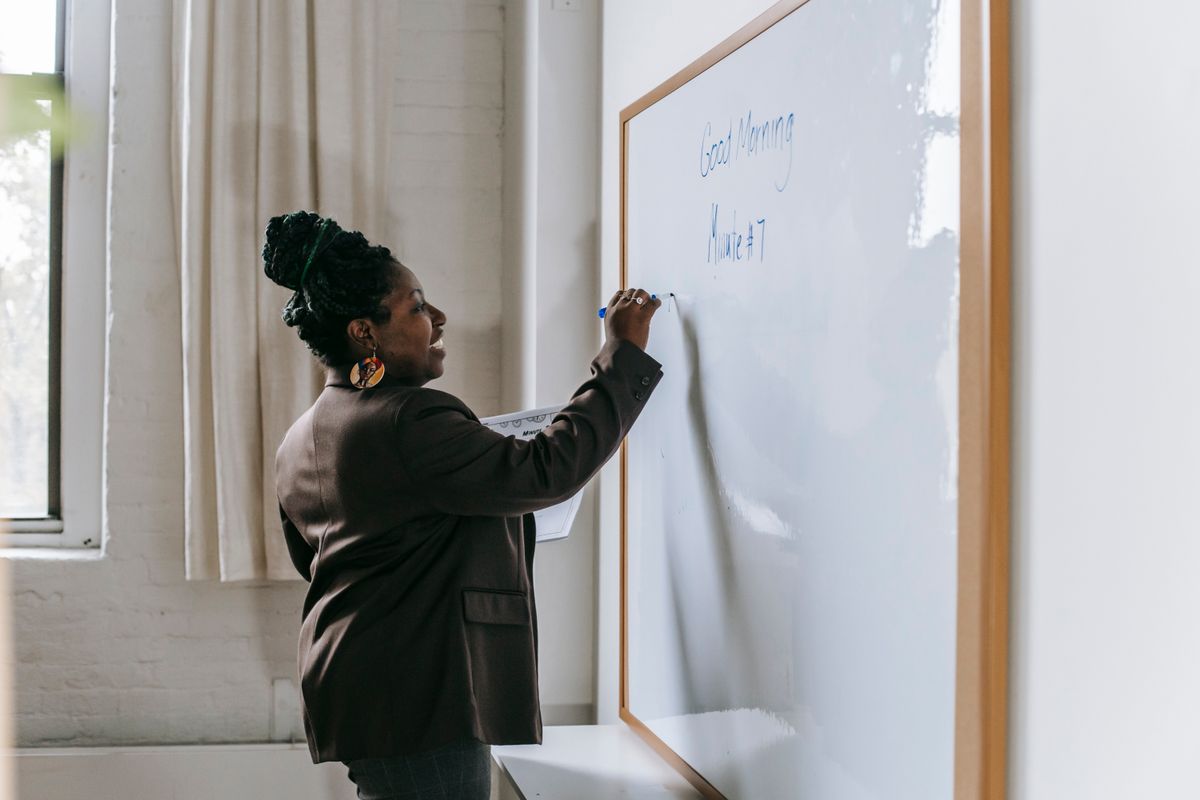 A confident teacher writing on a whiteboard while presenting a lesson in a modern classroom