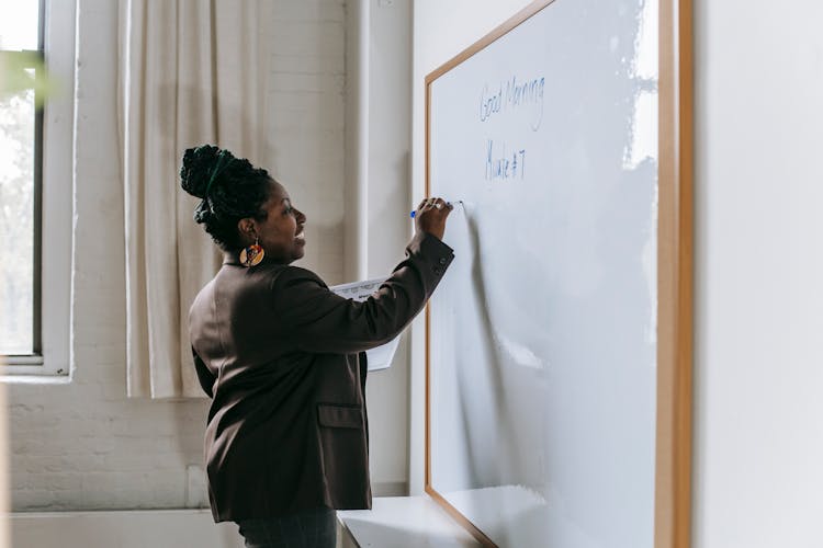 Cheerful Teacher Writing On Whiteboard In Classroom