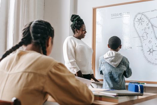 Black teacher with unrecognizable multiethnic pupils during biology lesson
