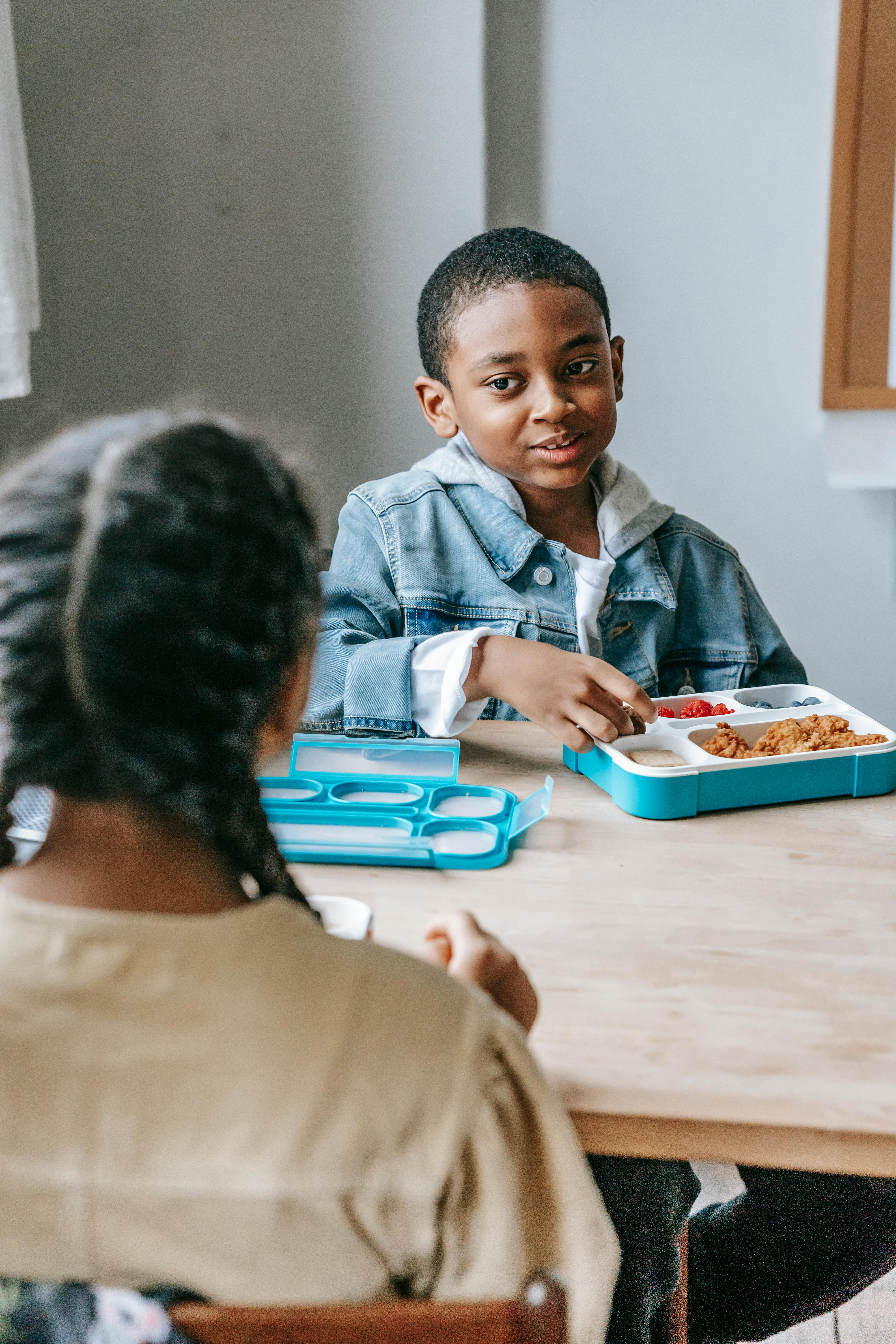 black schoolboy with lunch box talking to crop ethnic classmate