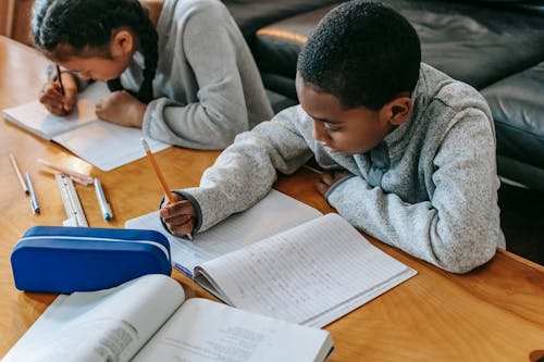 Crop multiethnic schoolchildren writing in copybooks at desk