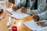 Crop pupils writing in copybook on desk