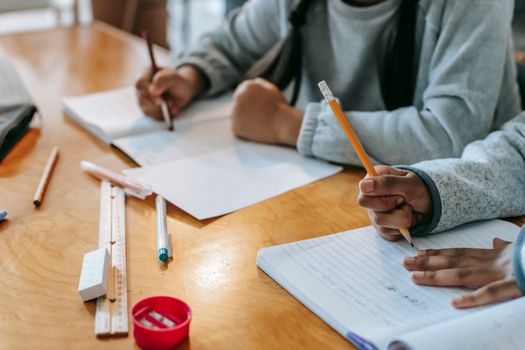 Crop pupils writing in copybook on desk