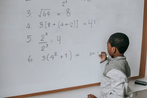 Free Black schoolboy solving math examples on whiteboard in classroom Stock Photo