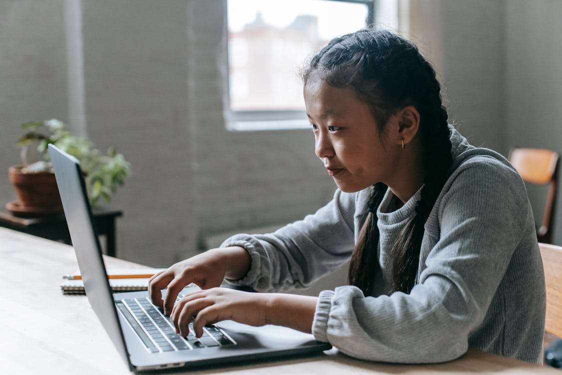 Free Focused Asian girl typing on laptop at home Stock Photo