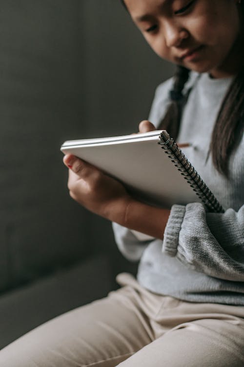 Free Crop serious Asian girl with pigtails wearing casual clothes sitting and preparing homework for school in copybook on blurred background Stock Photo