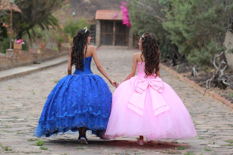 Girls Wearing Their Blue And Pink Ball Gowns While Holding Each Other's Hand