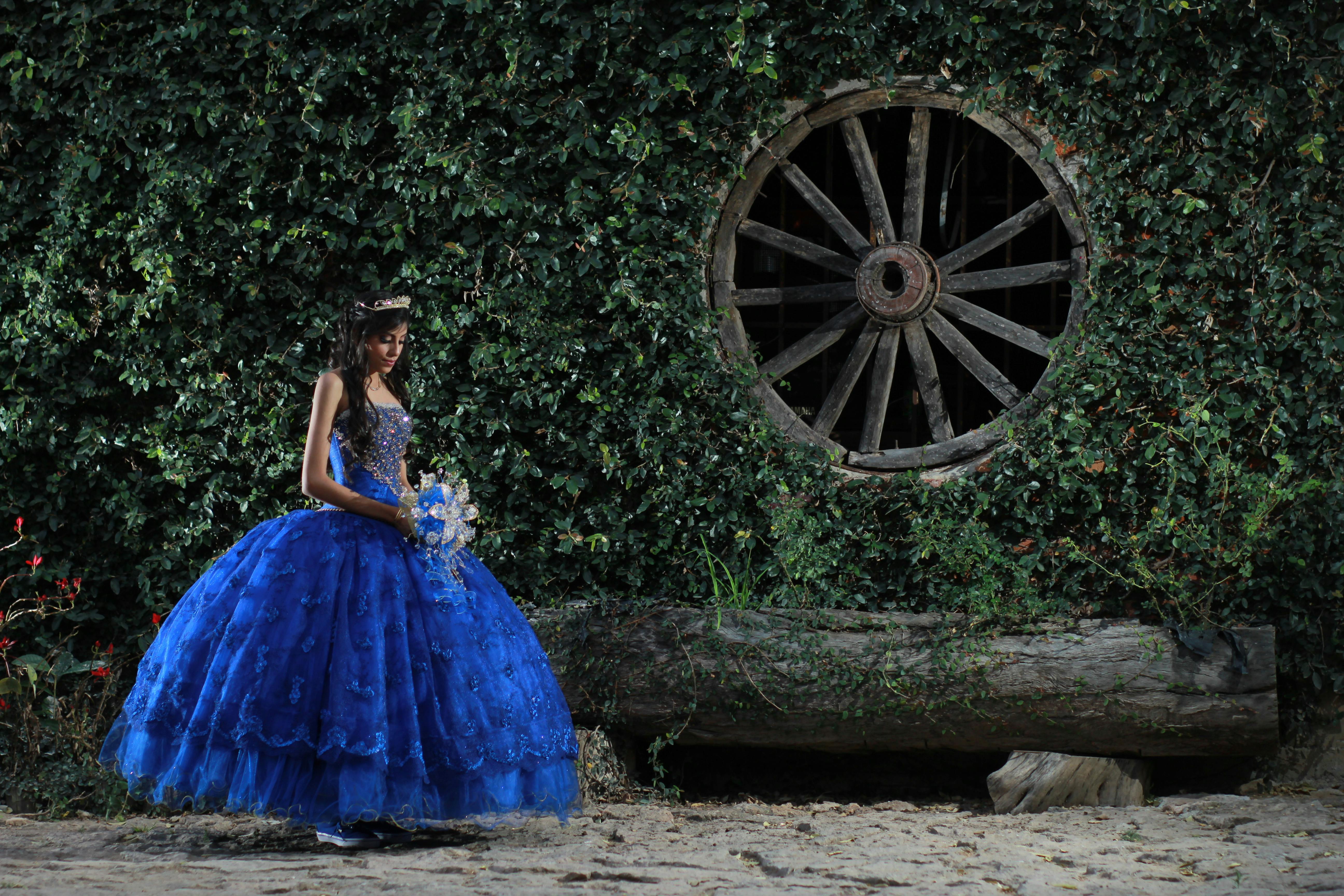 Woman in Blue Dress Standing Beside the Brown Wooden Wheel