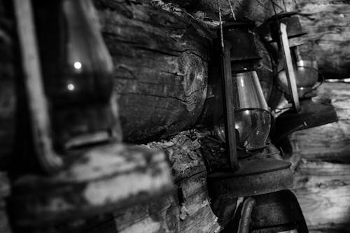 Black and white of old fashioned kerosene lanterns hanging on wooden wall in house in countryside