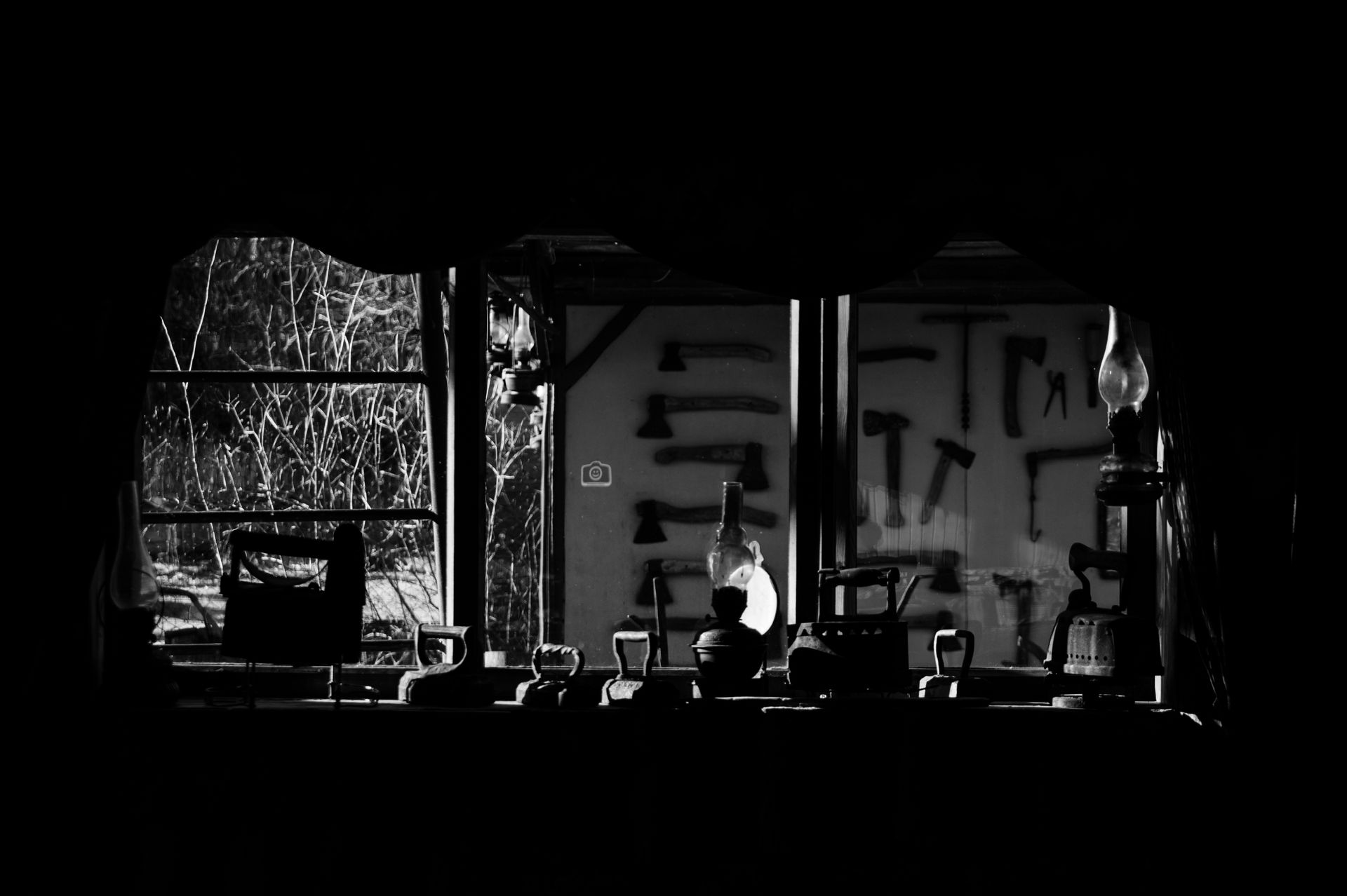 Black and white image of a vintage workshop interior featuring assorted tools and irons.