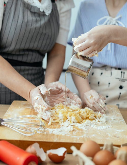 Crop woman pouring water from saucer into dough