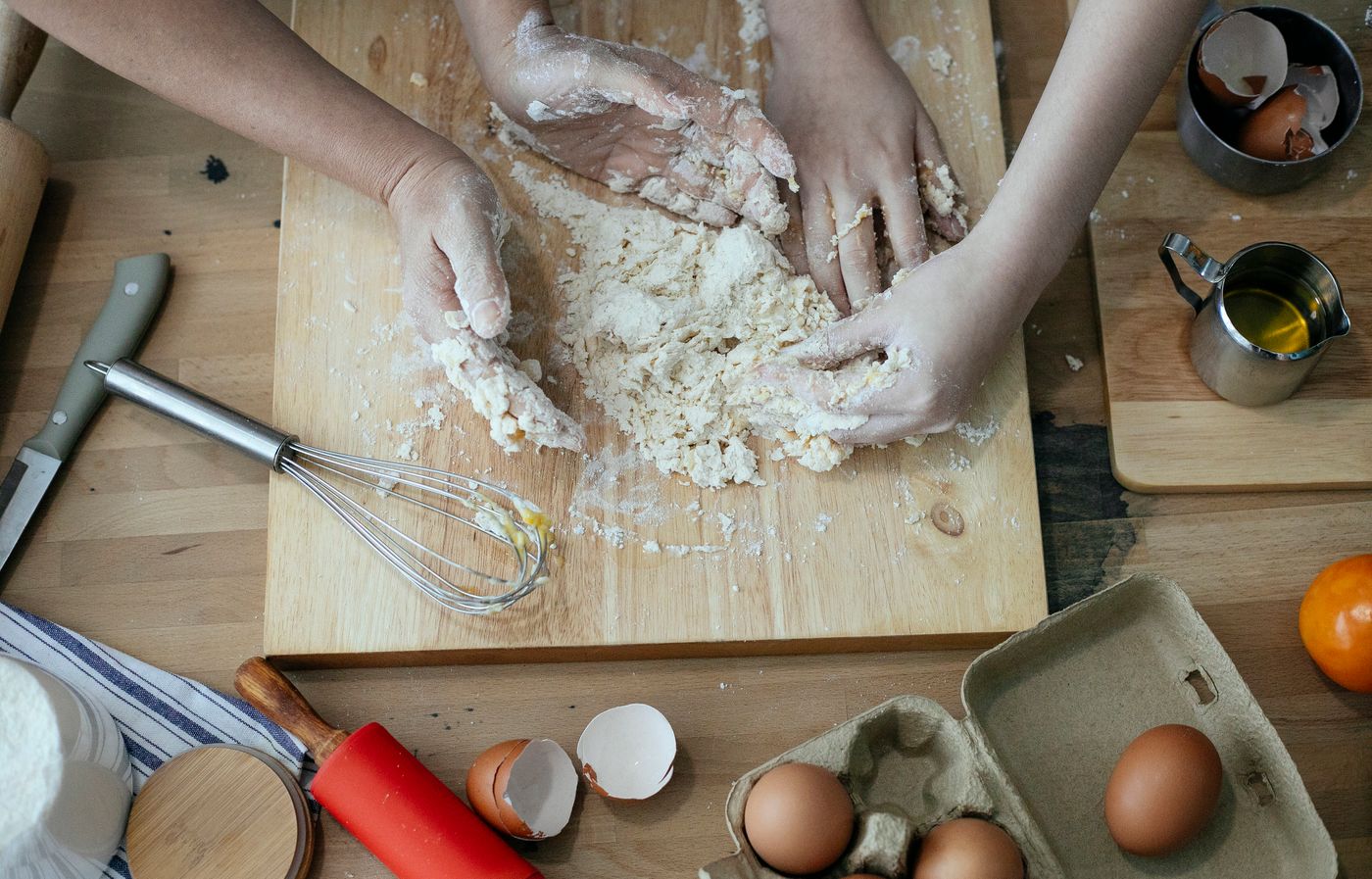 Las manos de dos mujeres amasando juntas sobre una tabla de madera, en una cocina.