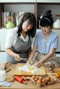 Delightful Asian woman and daughter mixing ingredients for dough together in kitchen