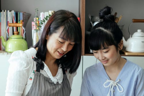 Cheerful Asian mother and daughter cooking together in kitchen