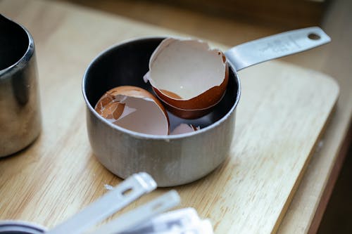 Free From above of stainless steel scoop with crashed eggshells placed on wooden table in kitchen in daylight Stock Photo