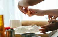 Crop young lady breaking eggs in flour for dough