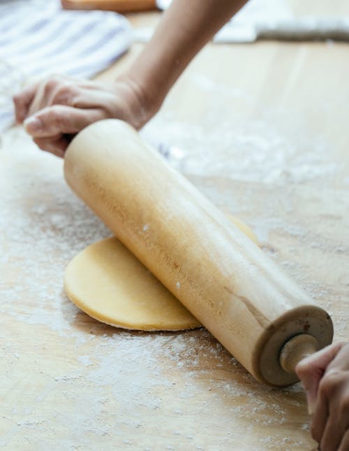 Crop anonymous lady rolling dough with pin on table on chopping board in kitchen in daylight