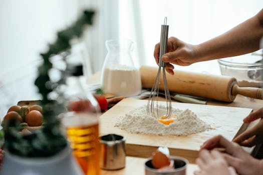 Crop unrecognizable ladies standing near table and whipping flour with egg for recipe on cutting board at home