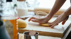 Female hands kneading fresh dough on wooden chopping board with flour in kitchen