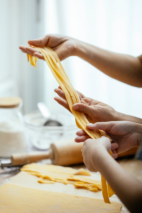 Female hands pulling together homemade raw long egg noodles while making oriental dish in kitchen
