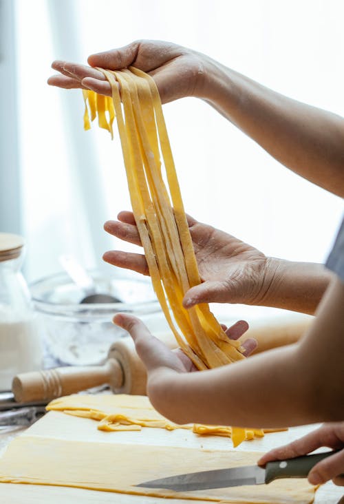 Free Female hands pulling long raw fresh homemade egg noodles cooking oriental dish in kitchen Stock Photo