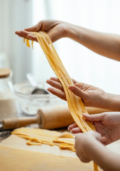 Female hands gently pulling homemade raw long noodles made with egg dough in kitchen