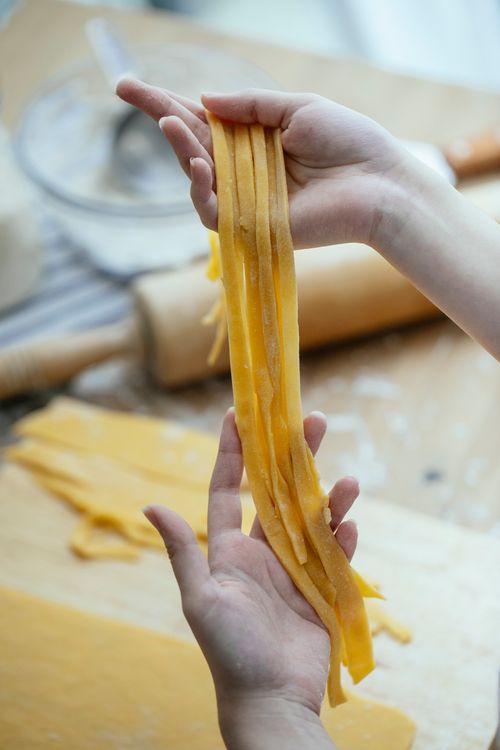 Free Female cook with raw uncooked long noodles made with homemade dough in kitchen Stock Photo