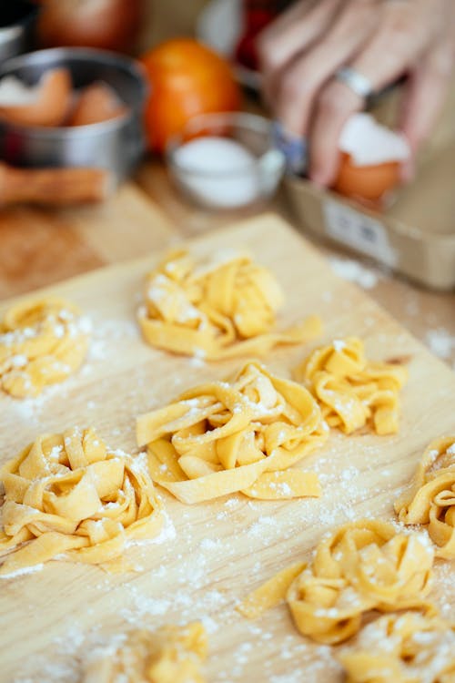 Homemade raw noodles sprinkled with flour on wooden chopping board on kitchen table