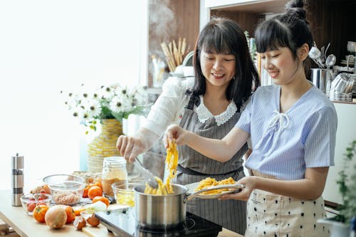 Free Happy mother and daughter cooking homemade long noodles in saucepan on electric hob in kitchen Stock Photo