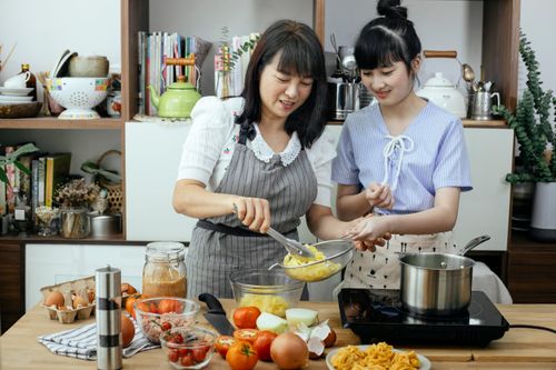 Free Young Asian teen with mother serving pasta from pan with boiling water cooking dinner together Stock Photo