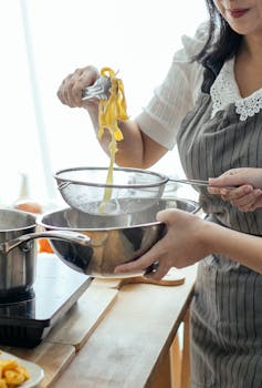 Woman straining fresh pasta in a colander over a pot in a home kitchen.