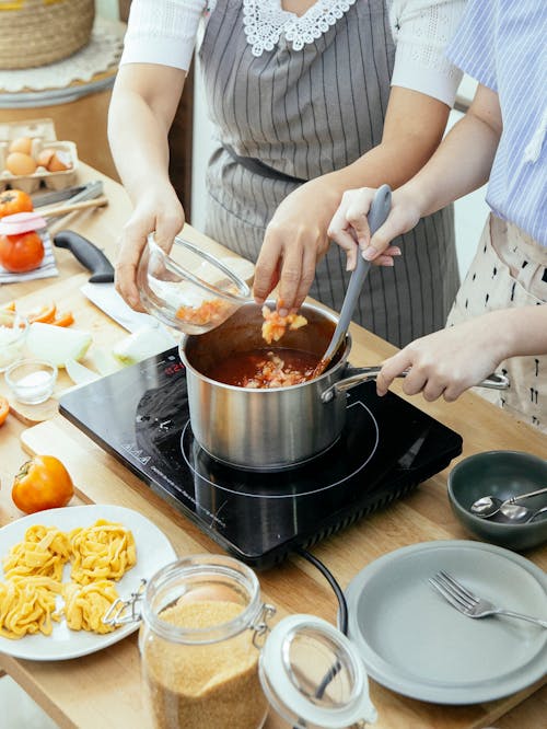 Free Anonymous women cooking pasta with sauce standing at table with ingredients in kitchen Stock Photo