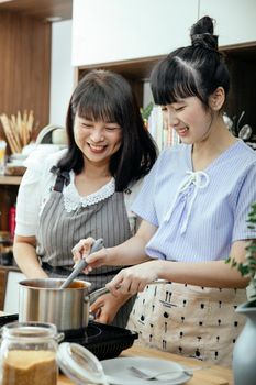 一对亚洲母女在自家厨房里上烹饪课，她们一边准备饭菜，一边微笑交流，增进感情