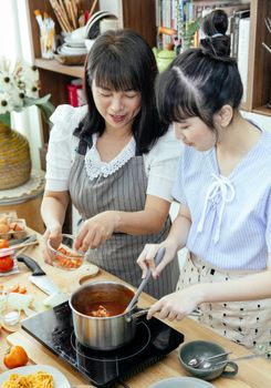 Ethnic women in aprons standing near table and cooking and stirring pasta at home