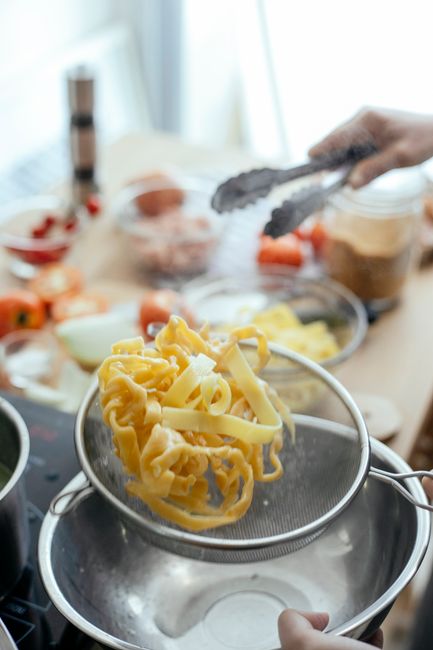 Pasta being strained through a colander over a pot of boiling water`
