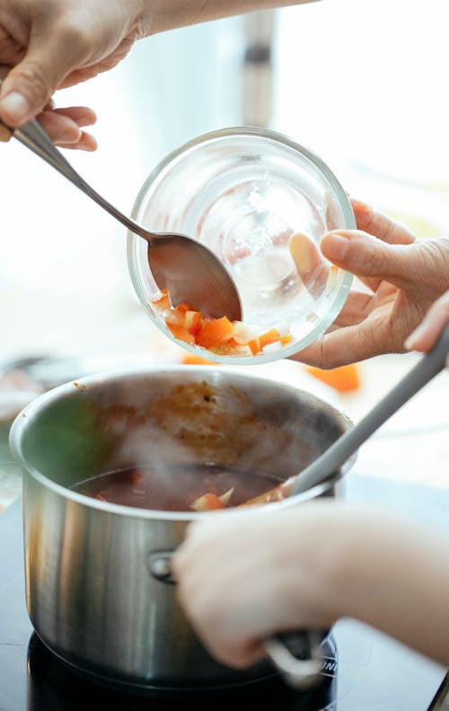 Free Anonymous cook adding fresh chopped tomatoes into pan with boiling chili while standing near stove in kitchen on blurred background Stock Photo