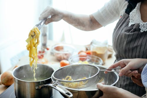 Free Crop anonymous females in aprons cooking delicious pasta using tongs and strainer in kitchen Stock Photo