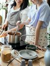 Crop unrecognizable cheerful females in aprons  standing near stove and cooking meal together in kitchen