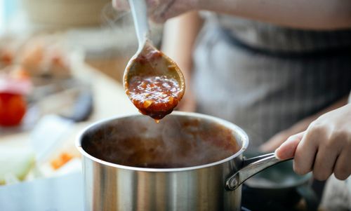 Free Crop anonymous females in aprons cooking sauce for pasta in saucepan in kitchen together Stock Photo