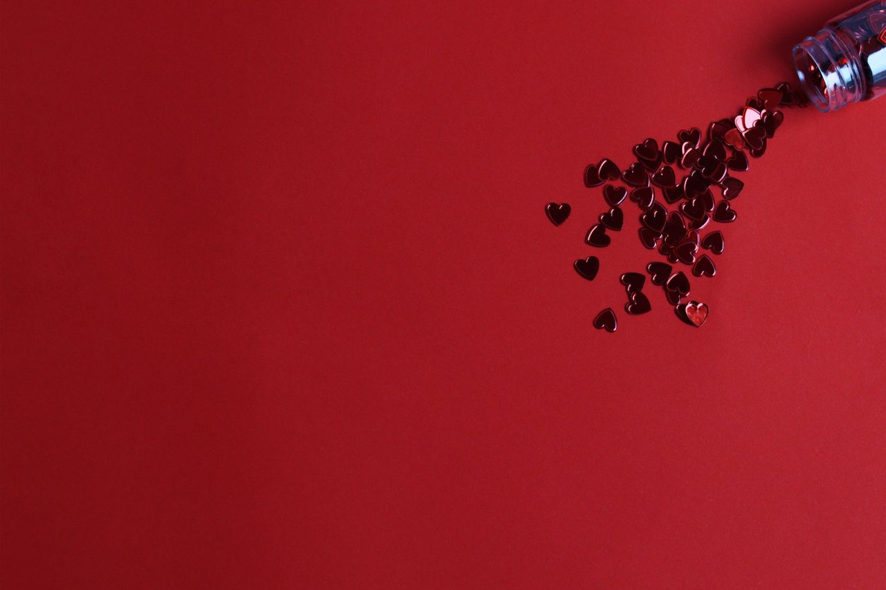 a scattered bottle of heart shaped confetti on a vibrant red backgroun