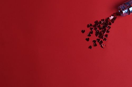 Free A scattered bottle of heart-shaped confetti on a vibrant red background with ample copy space. Stock Photo