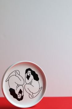 白色背景的陶瓷盘上，以极简主义风格描绘了两名女性的抽象插图
