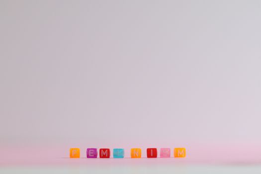 Vibrant letter blocks spelling 'feminism' on a pastel pink surface with a minimalist style.