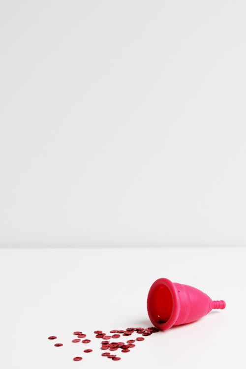 Free A red menstrual cup on a white background with scattered sequins symbolizing the menstrual cycle. Stock Photo