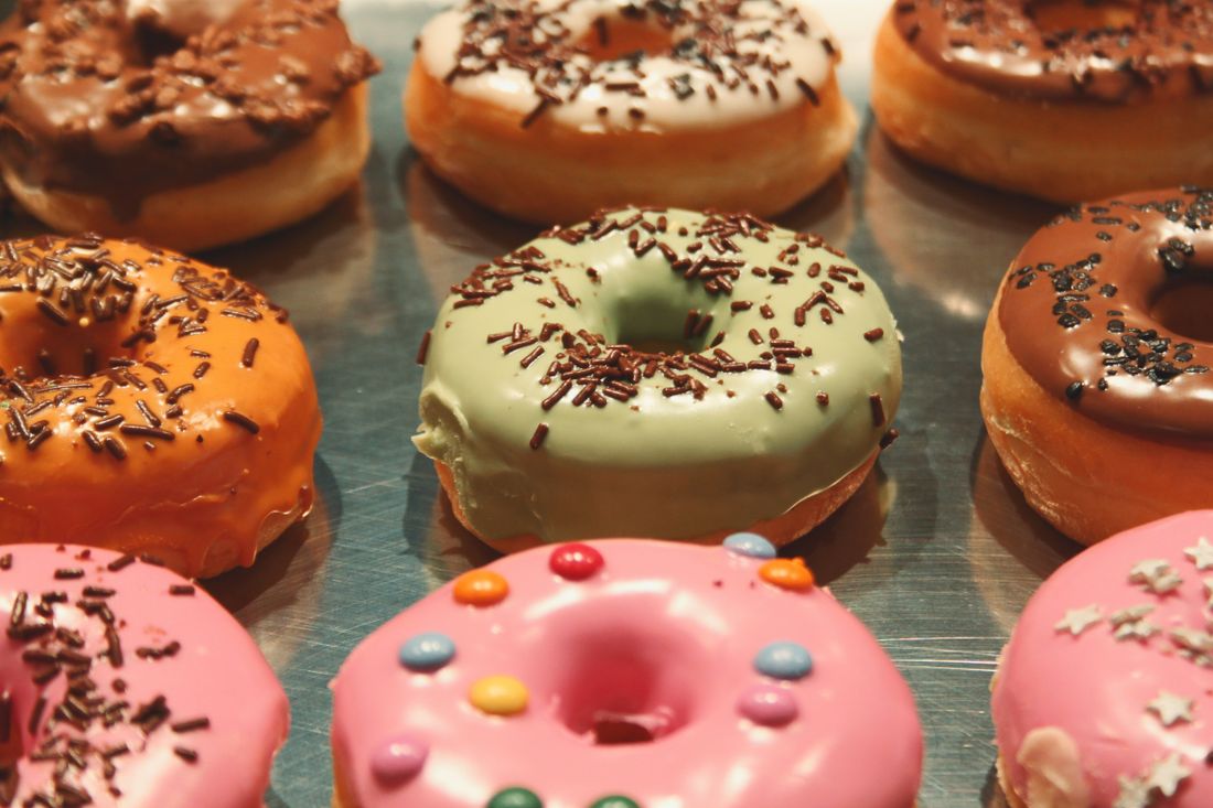 Rows of glazed donuts in pink, green, orange and chocolate with sprinkles on a tray