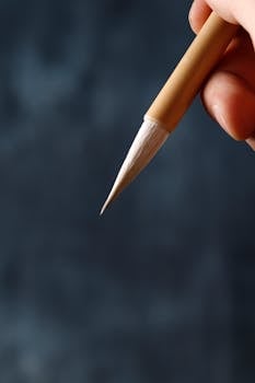Artistic capture of a fine brush held by a hand with a blurred dark background for creativity concepts.