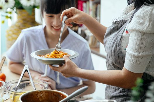 一对快乐的母女在室内一起烹饪意大利面，展示着她们的烹饪技巧