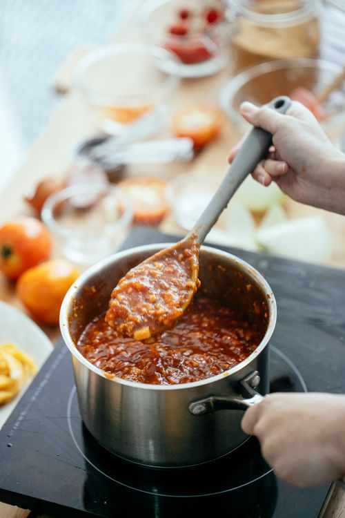 Free From above of crop anonymous female cook making sauce for pasta in saucepan on stove in kitchen Stock Photo