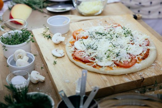 From above of dough with tomatoes and champignons topped with cheese prepared for pizza on wooden board