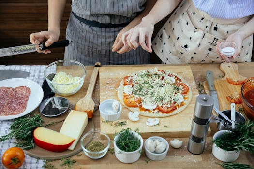From above of crop anonymous females in aprons making pizza together in kitchen